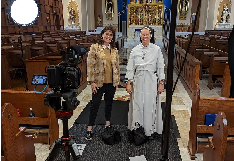 Dr. Karen Villa, a Catholic psychologist, and Sr. John Dominic smile at the camera. Behind them is the beautiful chapel of the Dominican Sisters of Mary, with statues of St. Dominic, St. Thomas Aquinas, St. Joseph, our Lady of Guadalupe, St. Catherine of Siena, and angels.