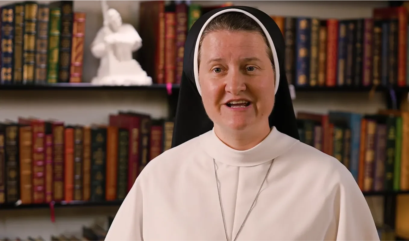 Dominican Sister in a study with books in the background speaking to the camera with a smile. 