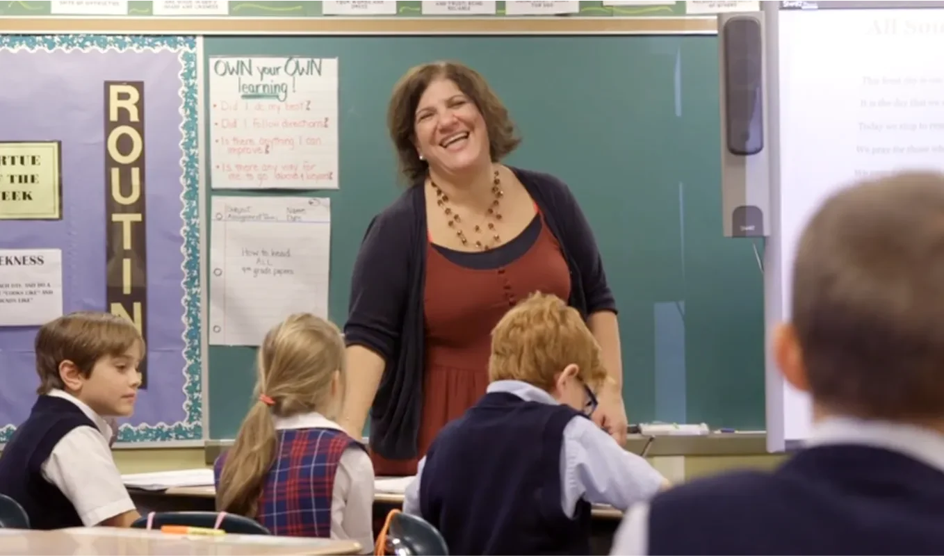 teacher-in-classroom-smiling-at-kids-as-teaching_compressed-1358x800